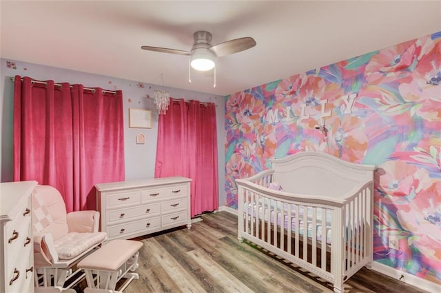 bedroom featuring ceiling fan, a crib, and wood-type flooring