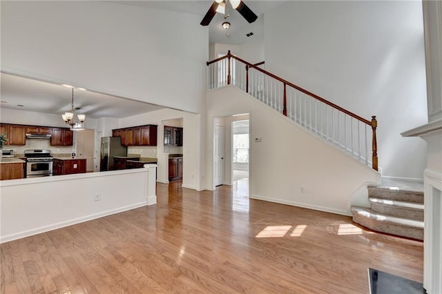 580 Hammersmith Dr, Suwanee, GA 30024 - unfurnished living room with light wood finished floors, a chandelier, ceiling fan, stairway, and a towering ceiling