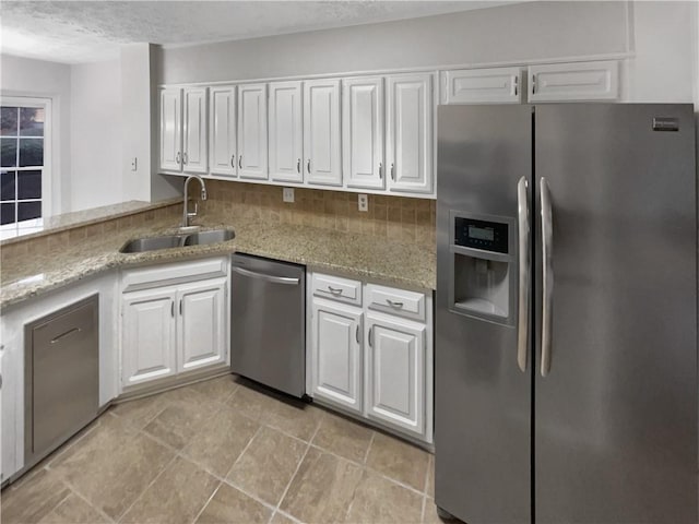 kitchen with appliances with stainless steel finishes, tasteful backsplash, white cabinetry, sink, and light stone countertops