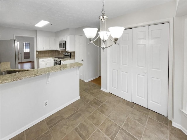 kitchen featuring light stone counters, a chandelier, hanging light fixtures, appliances with stainless steel finishes, and white cabinets