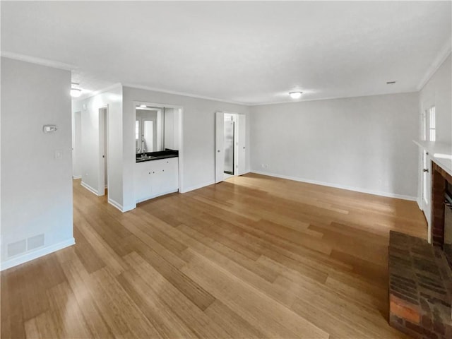 unfurnished living room with crown molding, a brick fireplace, sink, and light hardwood / wood-style flooring