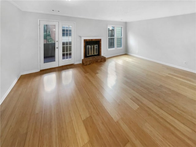 unfurnished living room with french doors, a brick fireplace, and light hardwood / wood-style flooring