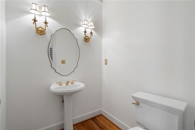 half bath with toilet, baseboards, and wood finished floors