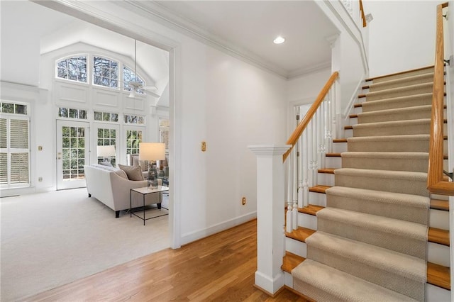 stairway with ornamental molding, wood finished floors, recessed lighting, baseboards, and a towering ceiling