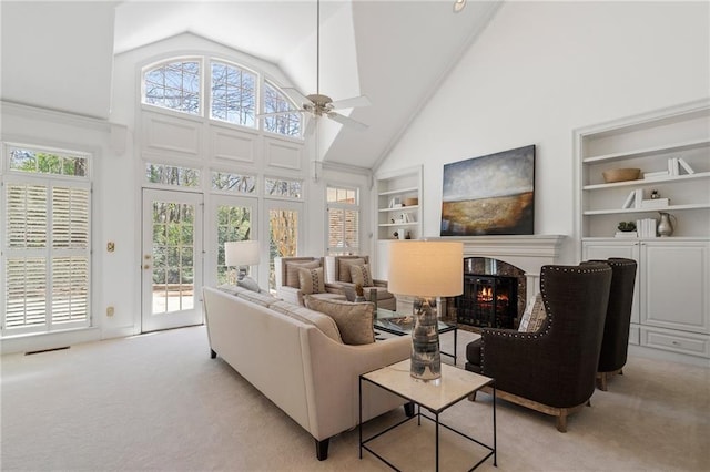 living room with a wealth of natural light, built in shelves, light colored carpet, and a warm lit fireplace