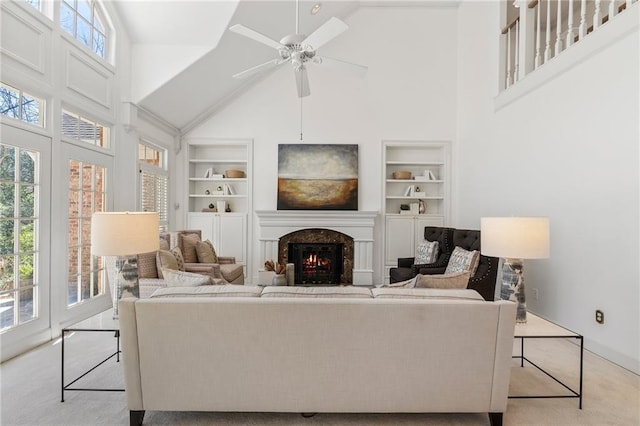 carpeted living area featuring built in features, a healthy amount of sunlight, ceiling fan, and a warm lit fireplace