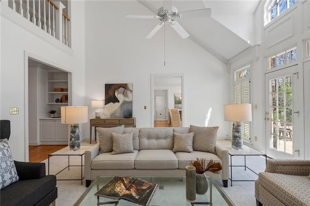 living room featuring a ceiling fan, built in features, wood finished floors, and a towering ceiling