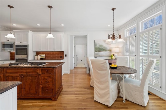 kitchen featuring an inviting chandelier, stainless steel appliances, white cabinetry, crown molding, and tasteful backsplash