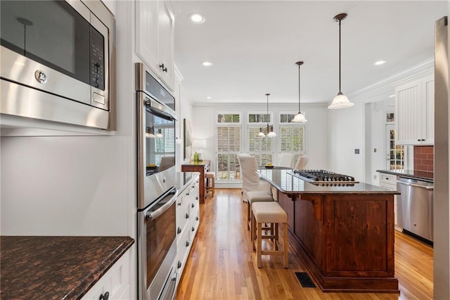 kitchen featuring white cabinets, light wood-type flooring, appliances with stainless steel finishes, and ornamental molding