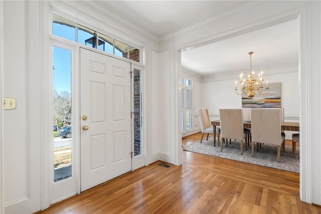 foyer with an inviting chandelier, wood finished floors, and crown molding