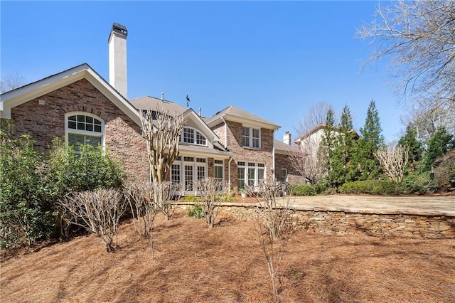 back of house featuring french doors, brick siding, and a chimney