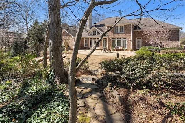 back of house featuring a patio area, brick siding, and a chimney