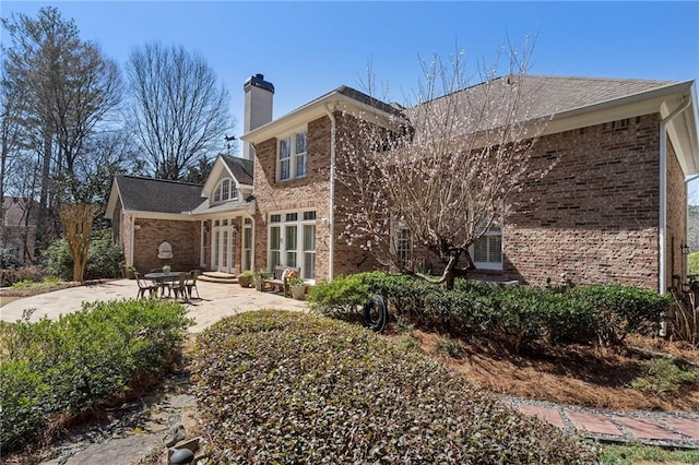 rear view of property featuring a patio, brick siding, and a chimney