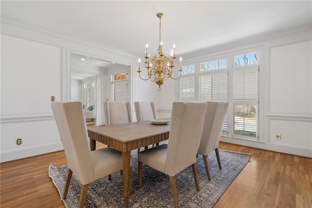 dining area featuring a decorative wall, a notable chandelier, ornamental molding, and light wood finished floors