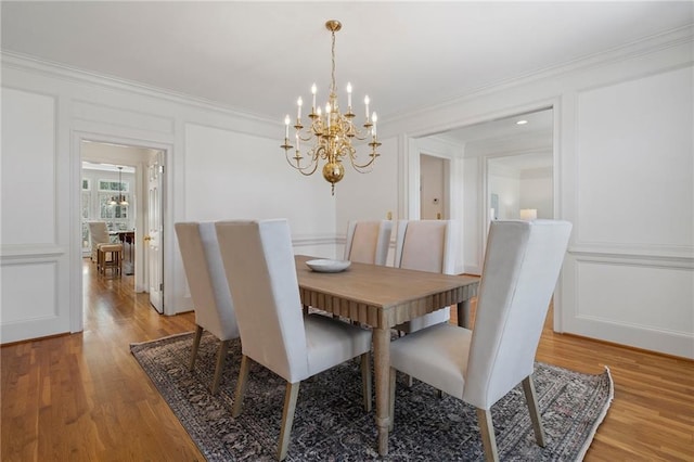 dining area featuring a notable chandelier, a decorative wall, light wood-style floors, and ornamental molding