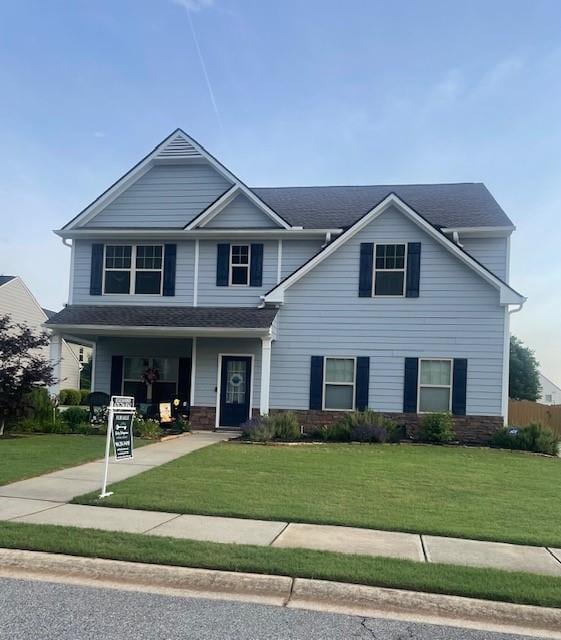 view of front of house featuring a front lawn, covered porch, and stone siding