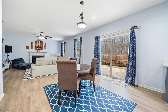 dining space featuring ceiling fan, a fireplace, baseboards, and wood finished floors