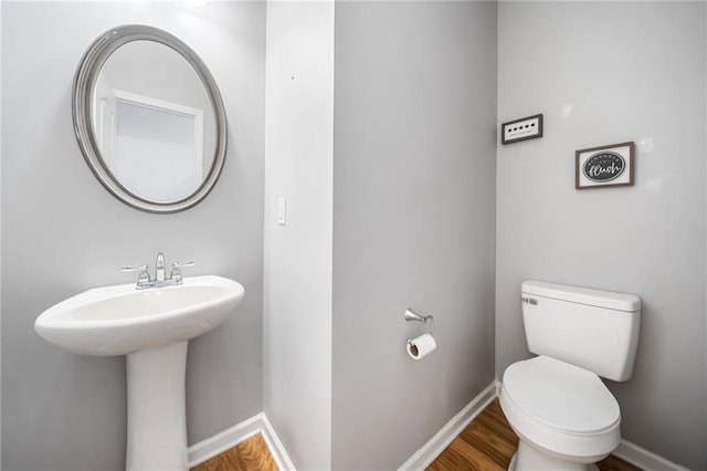 half bath with a sink, toilet, baseboards, and wood finished floors