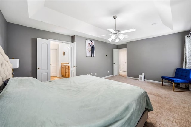 bedroom featuring a raised ceiling, light colored carpet, connected bathroom, and baseboards