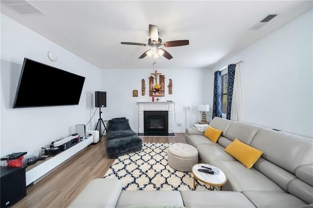 living area with a fireplace with flush hearth, visible vents, and wood finished floors