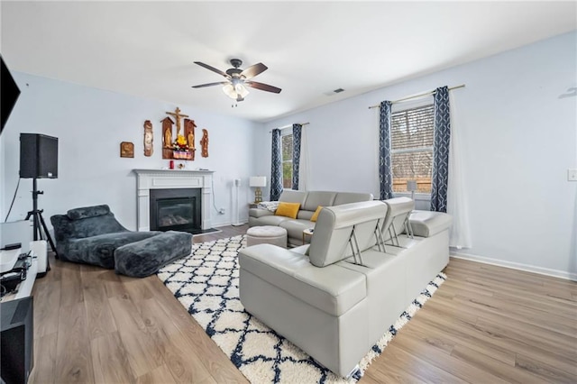 living area with baseboards, a fireplace with flush hearth, a ceiling fan, and wood finished floors