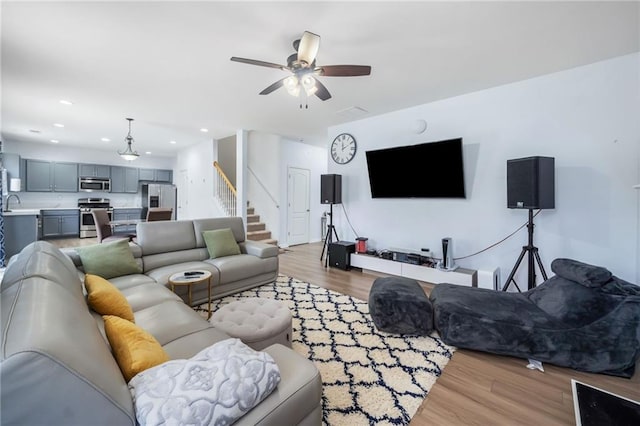 living room featuring stairs, light wood-type flooring, a ceiling fan, and recessed lighting