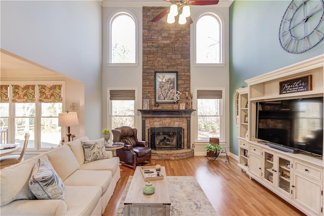 living room with a high ceiling, ceiling fan, light hardwood / wood-style flooring, and a fireplace