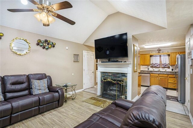 living room featuring light wood-type flooring, a textured ceiling, ceiling fan, a fireplace, and lofted ceiling