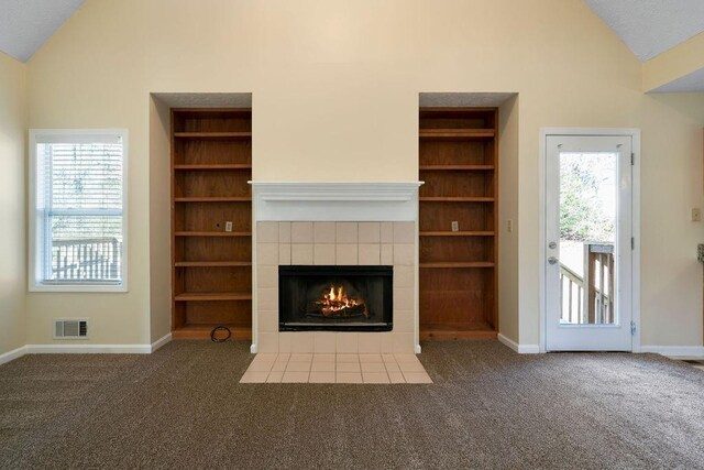 unfurnished living room with built in features, a tiled fireplace, vaulted ceiling, and dark carpet