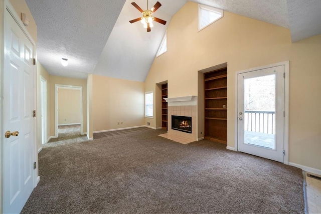 unfurnished living room featuring a textured ceiling, dark colored carpet, built in shelves, a tiled fireplace, and ceiling fan