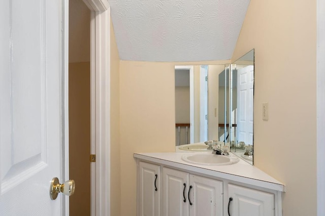 bathroom with a textured ceiling, lofted ceiling, and vanity