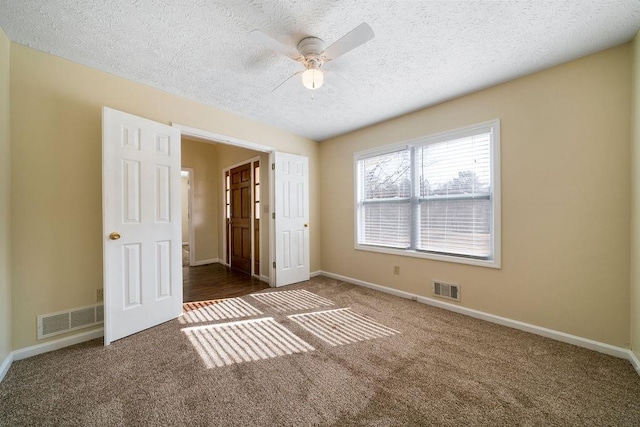 unfurnished bedroom featuring dark carpet, a textured ceiling, and ceiling fan