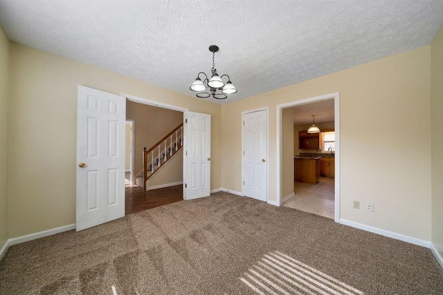 carpeted empty room with a textured ceiling and a chandelier