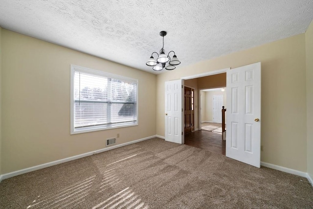 carpeted spare room featuring a textured ceiling and a chandelier