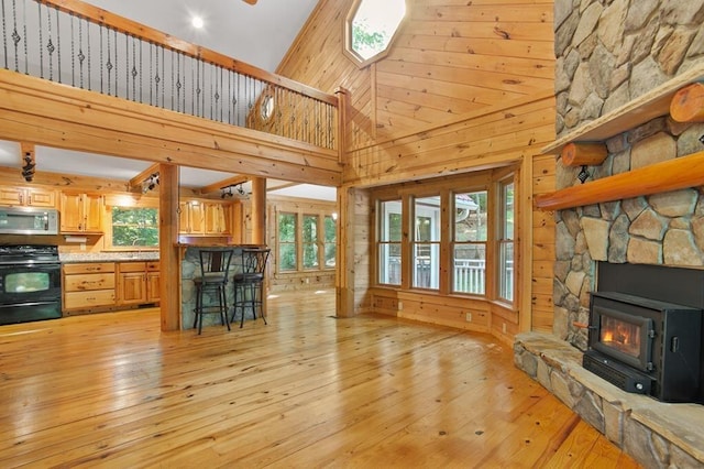 unfurnished living room featuring wood walls, high vaulted ceiling, a fireplace, and light wood-type flooring