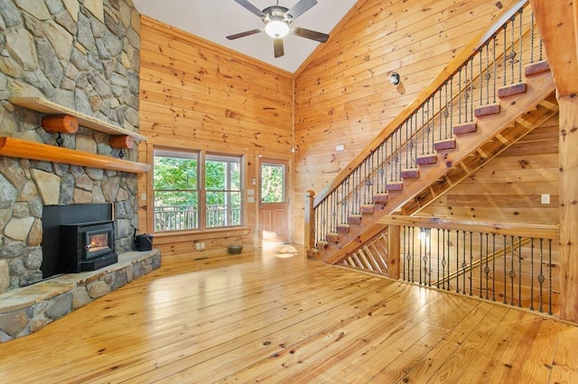 unfurnished living room featuring high vaulted ceiling, wood walls, light wood-type flooring, and ceiling fan