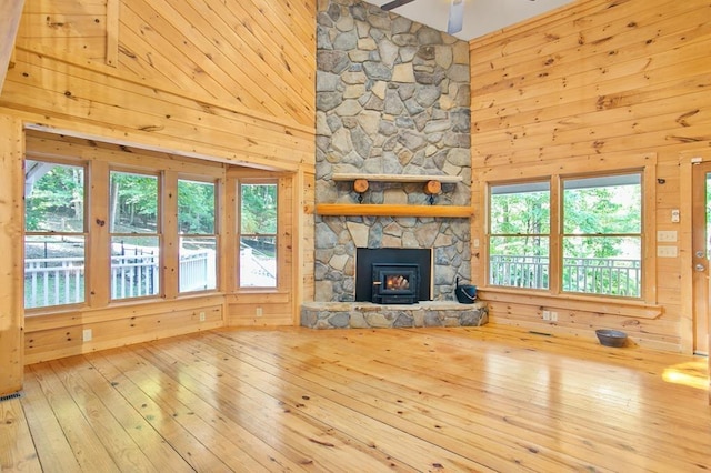 unfurnished living room featuring a stone fireplace, wood walls, and wood-type flooring