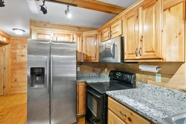 kitchen featuring wooden walls, track lighting, light hardwood / wood-style flooring, stainless steel appliances, and light stone countertops