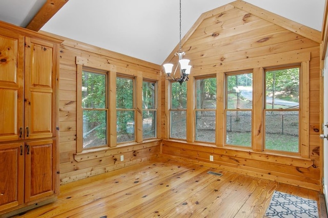 unfurnished dining area featuring wood walls, lofted ceiling, light hardwood / wood-style floors, and a notable chandelier