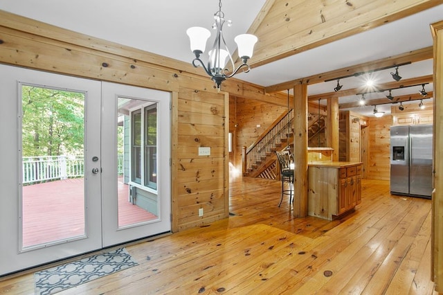 unfurnished dining area with a notable chandelier, light hardwood / wood-style flooring, french doors, and wooden walls