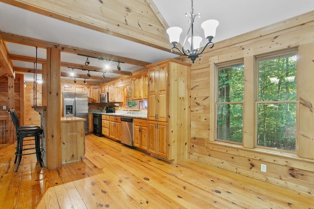 kitchen with a chandelier, stainless steel appliances, pendant lighting, wooden walls, and light hardwood / wood-style flooring