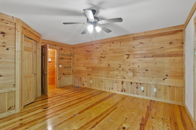 spare room with light hardwood / wood-style flooring, wooden walls, and ceiling fan