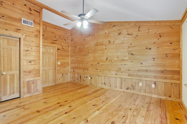 spare room with lofted ceiling, light hardwood / wood-style floors, wood walls, and ceiling fan