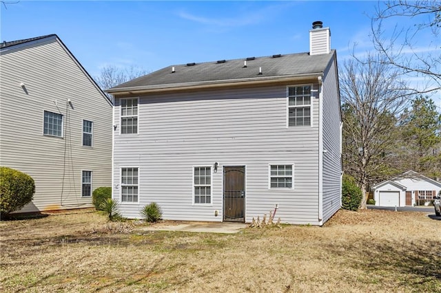 rear view of house with a chimney, a detached garage, a yard, a patio area, and an outdoor structure