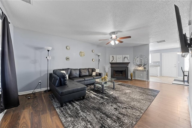 living room with visible vents, a fireplace, a textured ceiling, and wood finished floors