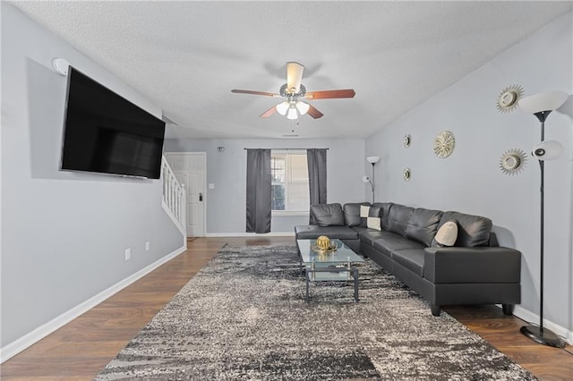 living area featuring ceiling fan, a textured ceiling, dark wood-type flooring, baseboards, and stairway