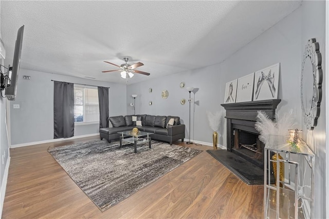 living room with baseboards, a fireplace with raised hearth, ceiling fan, wood finished floors, and a textured ceiling