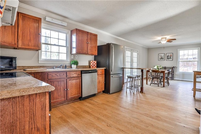 kitchen featuring sink, ornamental molding, stainless steel appliances, a textured ceiling, and light hardwood / wood-style flooring