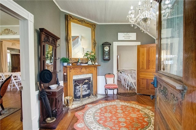 living area with a high end fireplace, an inviting chandelier, ornamental molding, and hardwood / wood-style flooring