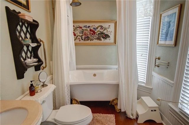 bathroom with wood-type flooring, a tub to relax in, toilet, and a healthy amount of sunlight